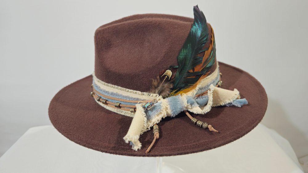 Nightwood — dark brown wide-brim hat with iridescent feathers and a turquoise talisman