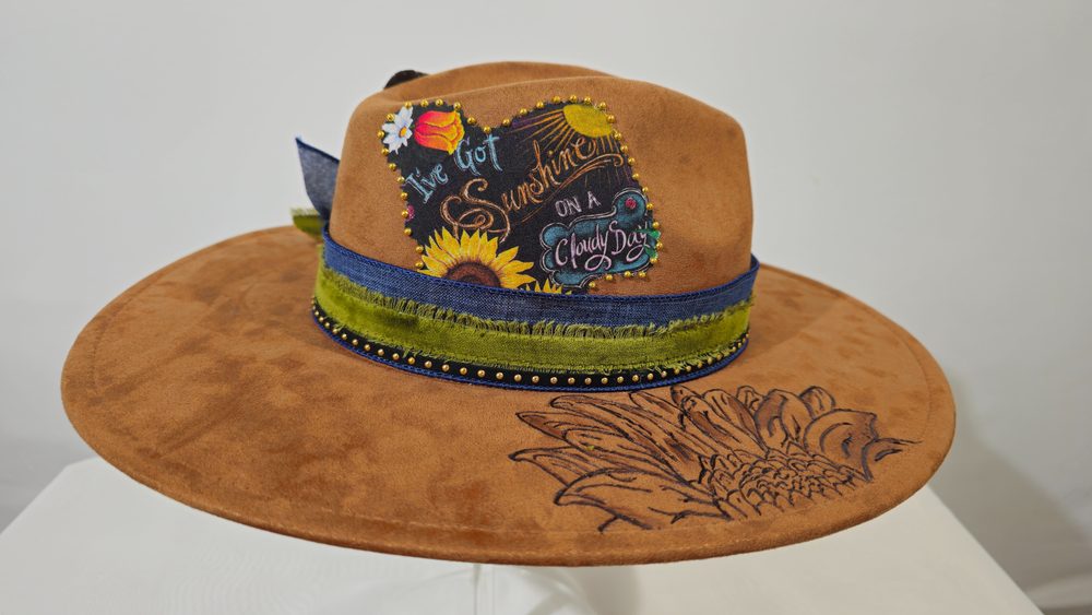 Sunroot — caramel brown wide-brim hat with an orange flower and feather accent