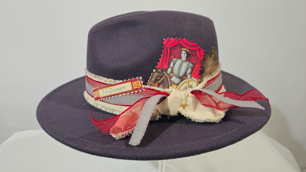 The Chariot — charcoal tarot hat with red, cream and gray textiles and a feather accent